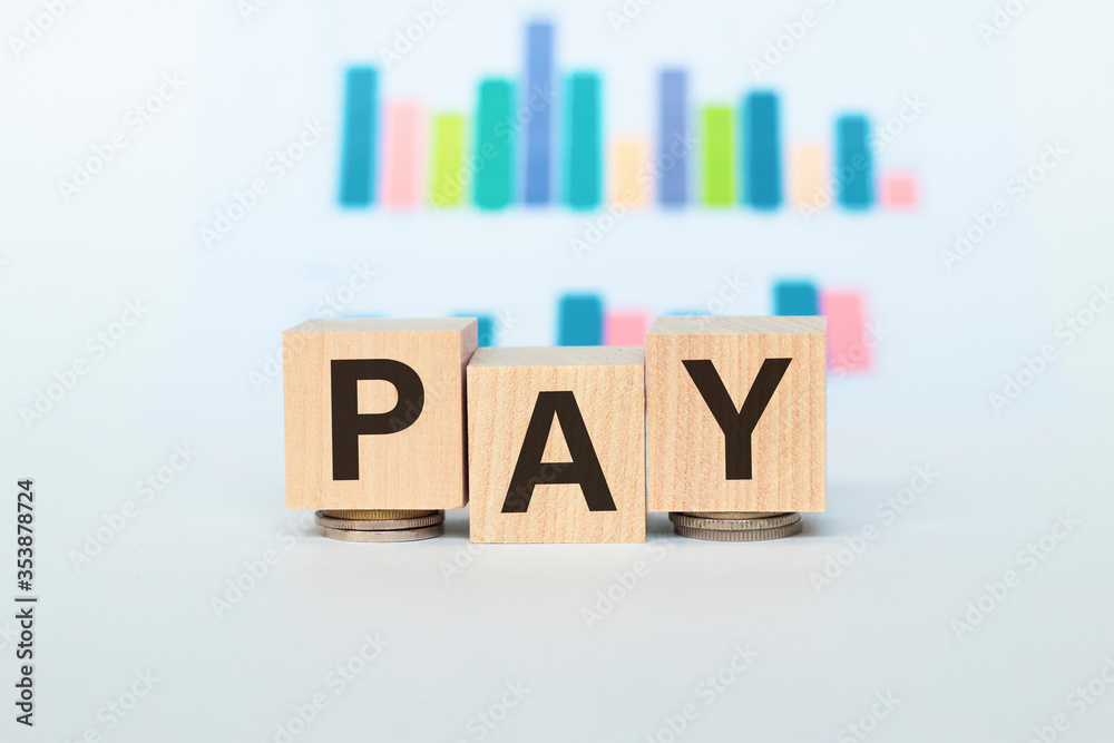 Wooden blocks with the text PAY and coins. Chart on background. Business and finance concepts. Wooden blocks with the text PAY and coins. Chart on background. Business and finance concepts.