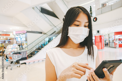 Traveler asian woman with mask and mobile phone in shopping mall for new normall lifestyle concept photo