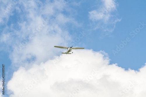 A small light light aircraft plane flies in the blue sky through white clouds. Horizontal orientation. 