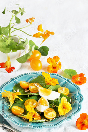 salad with nasturtium leaves and flowers of the plant. bright summer salad with edible  flowers and yellow tomatoes with egg, sunflower seeds.