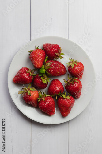 White dish filled with fresh strawberries on white wooden table right above vertical shot