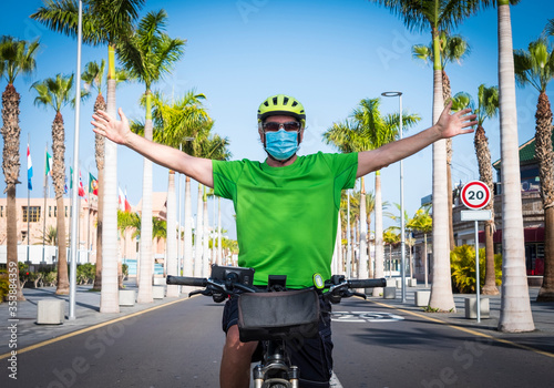 Man with open arms and medical mask riding his bicycle in the deserted road in Tenerife, Canary island. No people, no tourists because of the Covid-19 coronavirus. Palm trees and blue sky photo