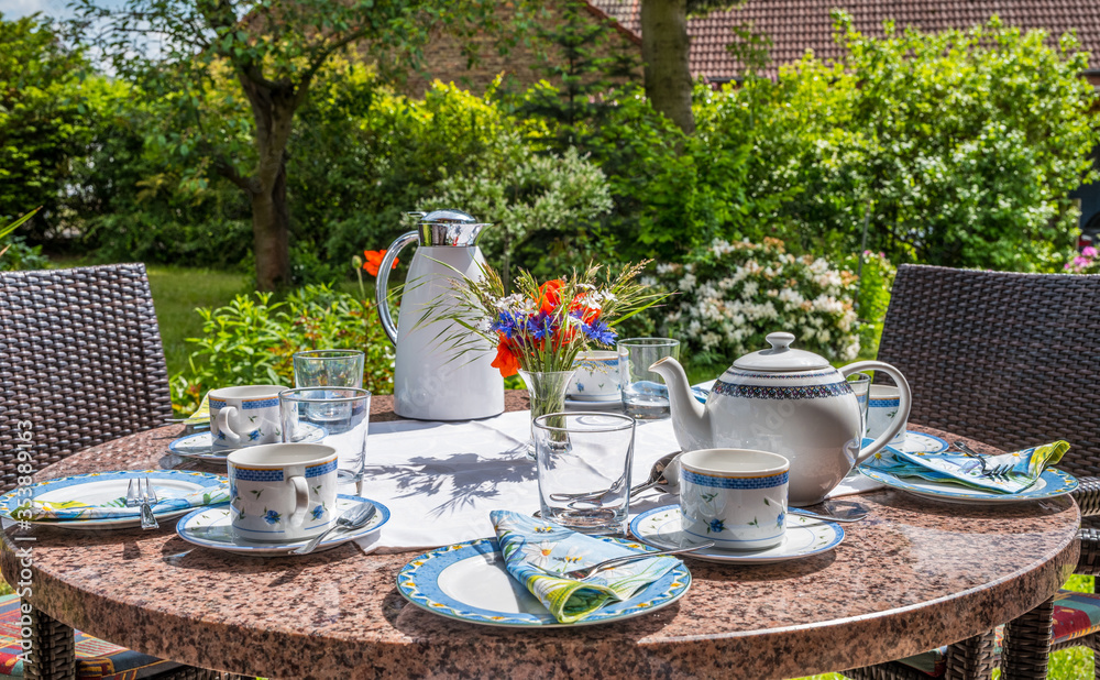 A beautifully decorated table with glasses, plates, cups and flowers in the garden invites you to a coffee break with friends