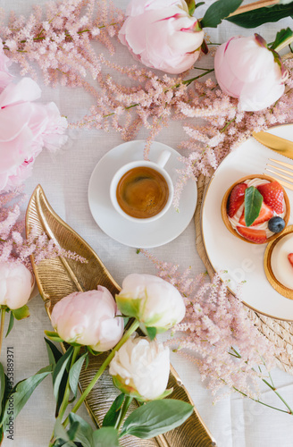 A cup of coffee  berry tartlet with fresh berries and peonies. Flat lay  composition. Coffee  dessert and flowers. Concept of coffee shop  cafe and flower shop.
