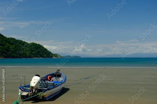 Fototapeta Naklejka Na Ścianę i Meble -  Tied down small Fishing boat on a wide expanse of empty beach on the Gulf of Nicoya in Costa Rica