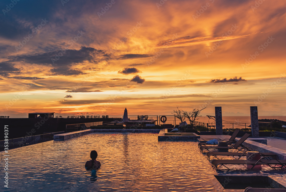 Silhouette of asian woman standing in the pool and looking to sunset view with chilling location on golden hour time.