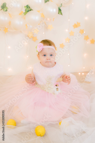 Cute little girl in a pink princess dress with a flower on her hair plays with wooden ballerinas among the golden stars on the background of a large white wooden moon and balloons. Children's decor. 
