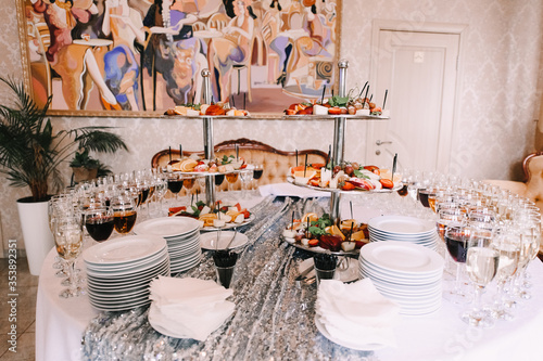 Shelve with fruit: grapes, strawberries, orange, peach, cheese. Reception, catering, clean dishes, glasses with wine, champagne, juices. The table is covered with a white and silver tablecloth