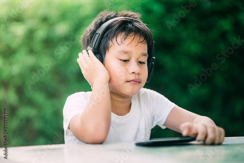 Asian boy is sitting listening to music by wearing headphones in the garden via smartphones