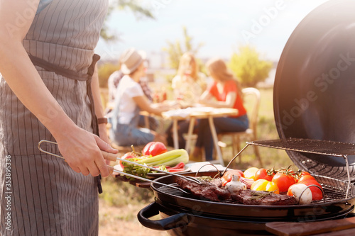 Man cooking meat and vegetables on barbecue grill outdoors, closeup photo
