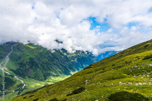 Green Austrian Alps covered with grass and forests under white clouds