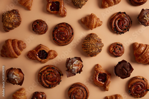 Above shot of tasty appetizing confectionery to satisfy your sweet tooth. Pastry with fillings and raisin buns, chocolate muffins, croissants on beige background. Fresh high calories bakery products © Wayhome Studio