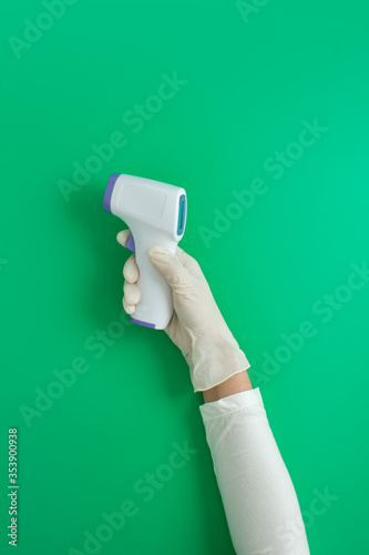 Human hand wearing surgical glove checking body temparature on green background