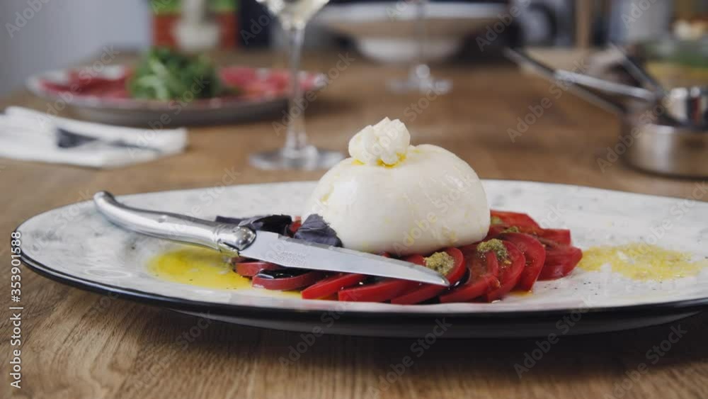 Burrata with tomato and basil. A beautiful dish and a glass of wine are standing on the table at the restaurant. Burrata dish served by the restaurant. Beautiful composition with a dish of wine. Burrata with tomato and basil. A beautiful dish and a glass of wine are standing on the table at the restaurant. Burrata dish served by the restaurant. Beautiful composition with a dish of wine.