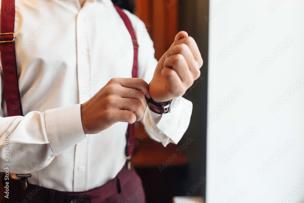 A groom putting on cuff-links as he gets dressed in formal wear. A man straightens cufflinks. Groom's suit