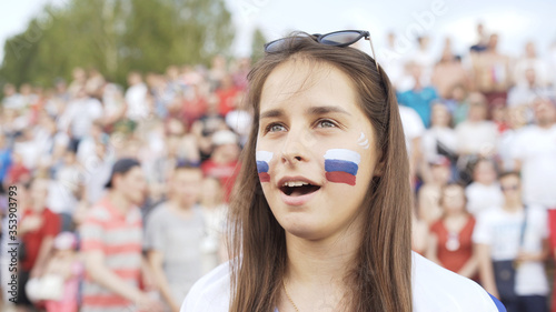 Portrait of Pretty Female football fan sings Russian national anthem cheering at match, supporting football team. Young woman listening and singing national anthem before football match at stadium