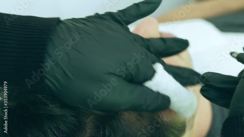 Close up of cosmetologist making permanent makeup. Microblading procedure. High quality close-up 4k slow motion video of a man laying on a couch during the esthetician brow microblading treatment.