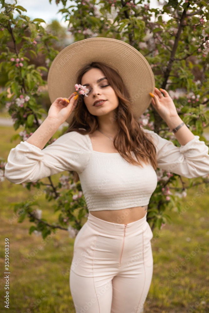 Long-haired girl in a hat in an Apple orchard in spring