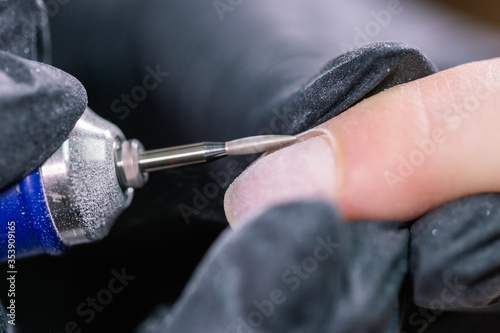 Hardware manicure in a beauty salon. Female manicurist is applying electric nail file drill to manicure on female fingers. Mechanical manicure close-up. Concept body care.