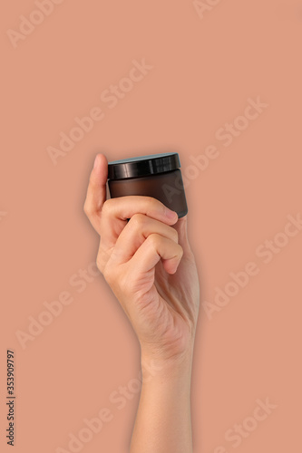 hand hold cosmetic skincare cream amber glass jar on pink background.