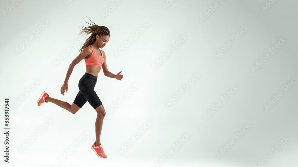 No limits. Full length of young african woman with perfect body in sports clothing jumping against grey background while training in studio