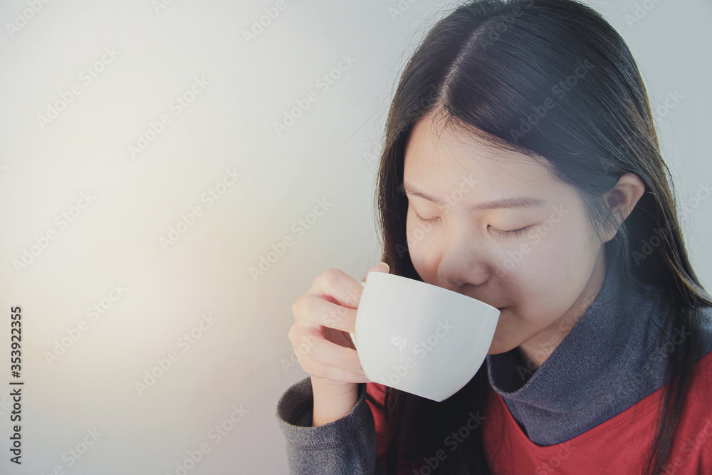 Beautiful asian woman enjoys drinking a cup of hot coffee during winter time. White plain background, space for text. Beautiful asian woman enjoys drinking a cup of hot coffee during winter time. White plain background, space for text.