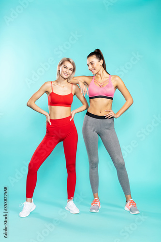 Wallpaper Mural Ready for workout. Full length of two young and attractive sporty girls in sportswear looking at camera and smiling while standing against blue background. Sport and fitness Torontodigital.ca