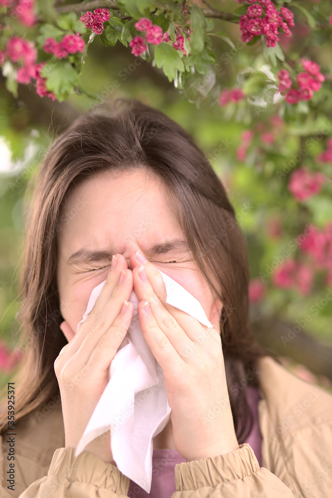 Young girl is blowing her nose near spring tree in bloom. Health and medicine concept Young girl is blowing her nose near spring tree in bloom. Health and medicine concept