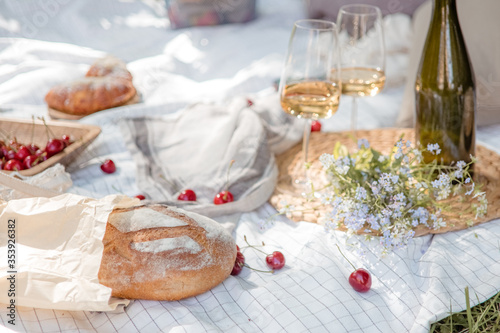 Aesthetic picnic outdoors with wine glasses bread berries and flowers. Rustic picnic with neutral tones colours. 