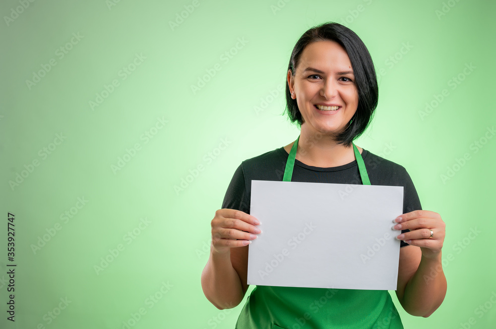 Female cook with green apron and black t-shirt holding a white paper Female cook with green apron and black t-shirt holding a white paper