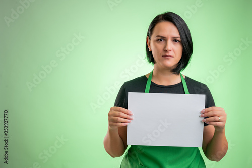 Female cook with green apron and black t-shirt holding a white paper photo