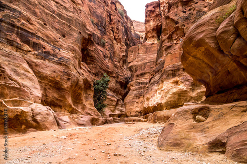  A winding road on a hot summer day with red rocks to the facade of Petra in Jordan.