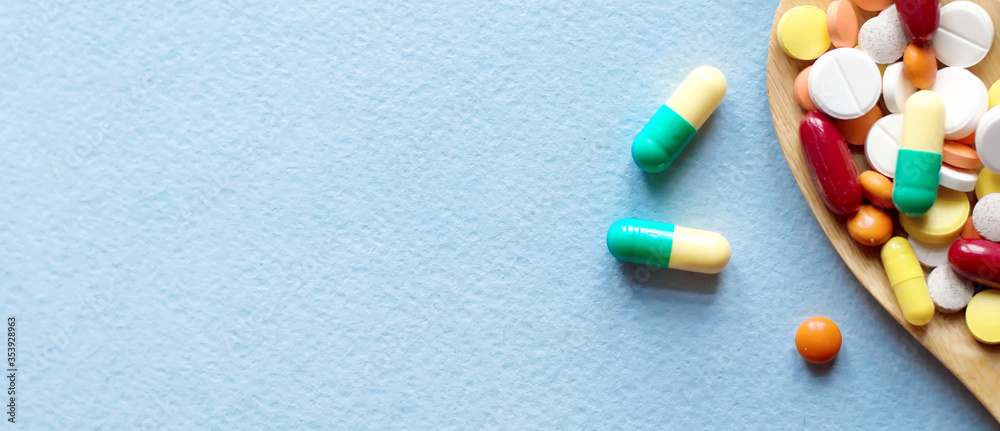 pharmaceutical medicine pills, tablets and capsules in a wooden spoon on a blue table. Medical and health concept. Top view pharmaceutical medicine pills, tablets and capsules in a wooden spoon on a blue table. Medical and health concept. Top view