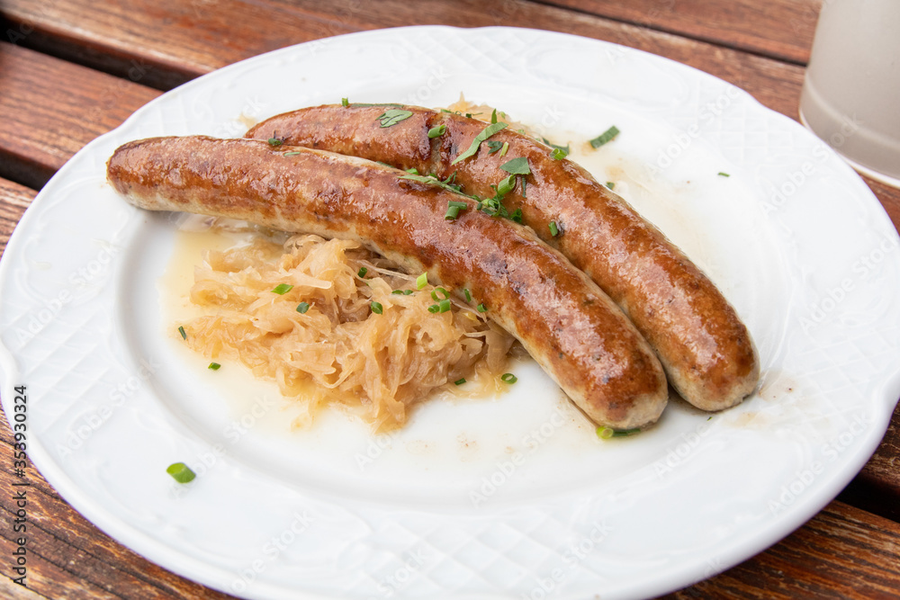Bratwurst sausage (Brätwurst, brät, Wurst)and sauerkraut traditional German dish/food with garnish/chives on a white plate and wooden table