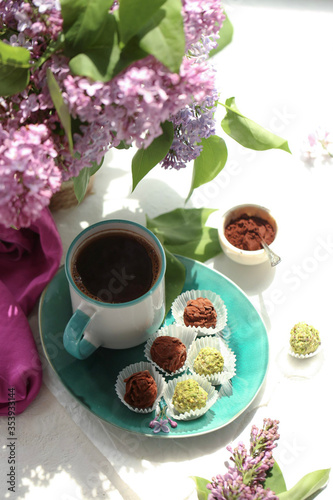 A plate with chocolates, a cup of tea and a bouquet of lilac flowers. 