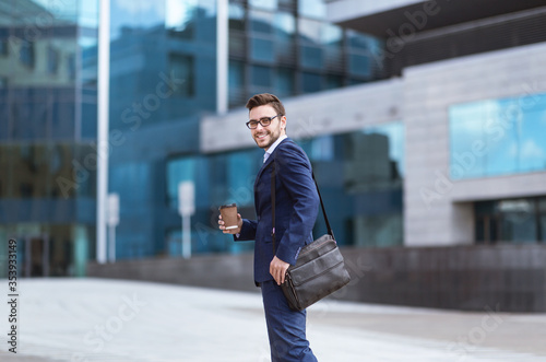 Handsome businessman with takeaway coffee going to his office building in morning