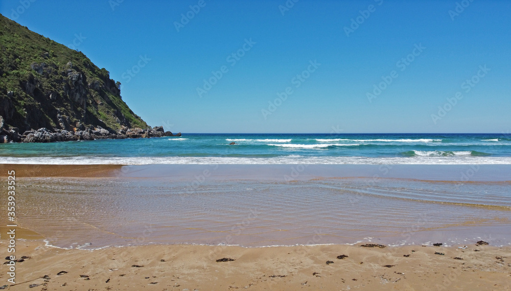Orilla de la playa, pequeñas olas rompen en la arena, un promontorio se levanta al final de la playa