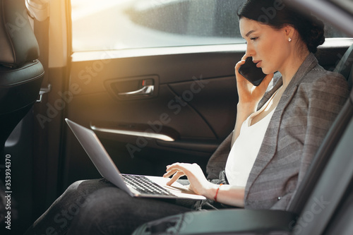 Young businesswoman in suit talking to investors while sitting in a car and checking information through a laptop.