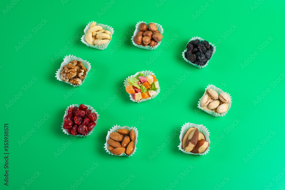 A serving of assorted candied fruit, dried cherries, almonds, raisins, walnuts and hazelnuts in paper muffin cups on a green background. A serving of assorted candied fruit, dried cherries, almonds, raisins, walnuts and hazelnuts in paper muffin cups on a green background.