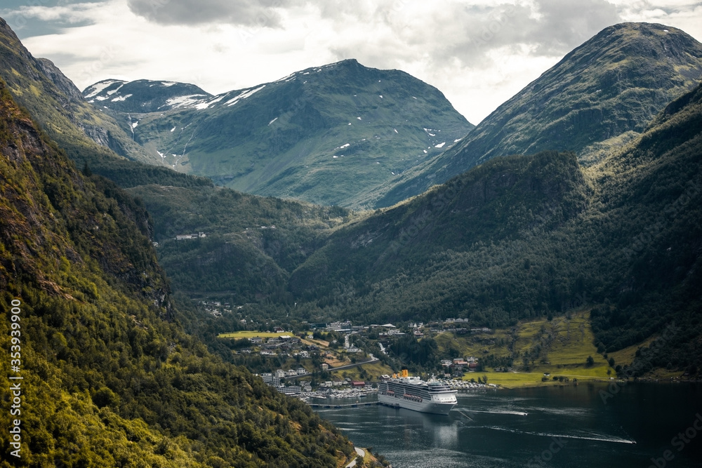 Trip to Norway. Panoramic view of Geiranger town and mountain Dalsnibba with big ferry on fjord from the Eagle's road in the cloudy summer day