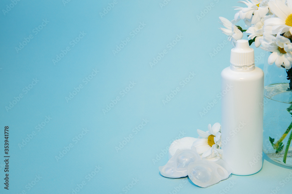 The contact lens change kit is next to a bunch of daisies. On the blue table are blisters with lenses, cotton pads, lens solution and chamomile. The background is blue. There is space for text. The contact lens change kit is next to a bunch of daisies. On the blue table are blisters with lenses, cotton pads, lens solution and chamomile. The background is blue. There is space for text.