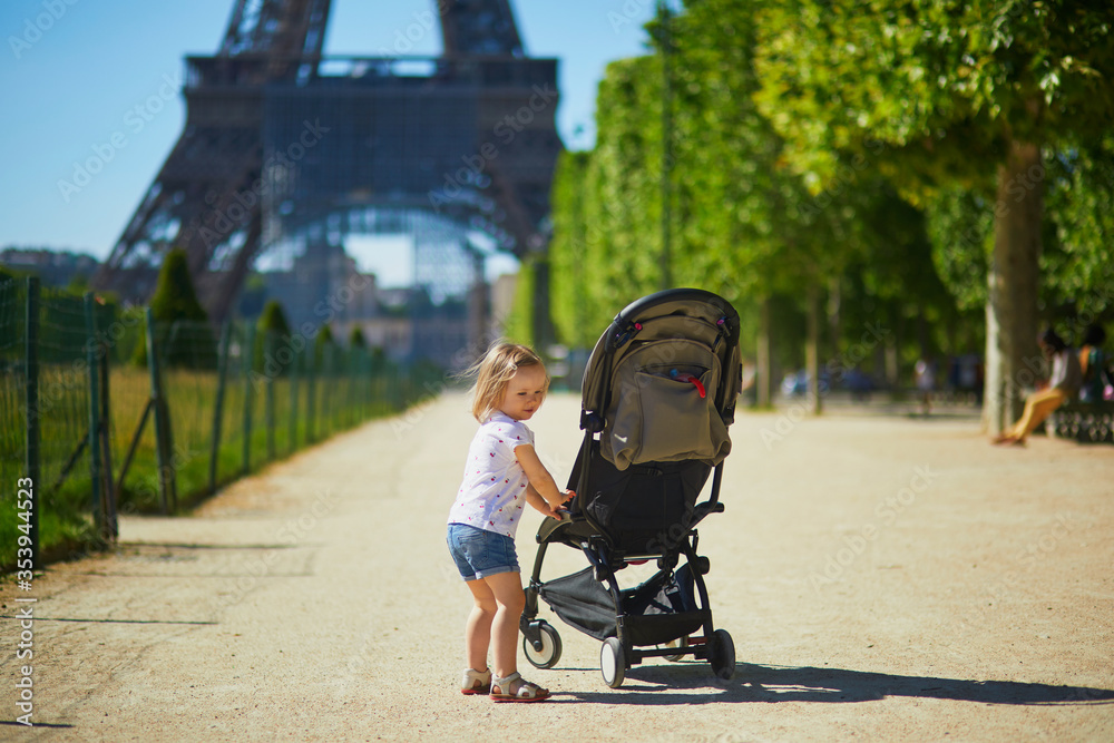 Obraz premium Cheerful toddler girl pushing stroller near the Eiffel tower in Paris, France