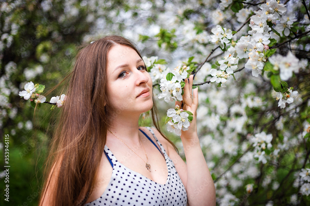 A pretty girl poses in the garden near a blooming Apple tree with white flowers. Spring garden. Beautiful women's hair. Portrait of a beautiful model.