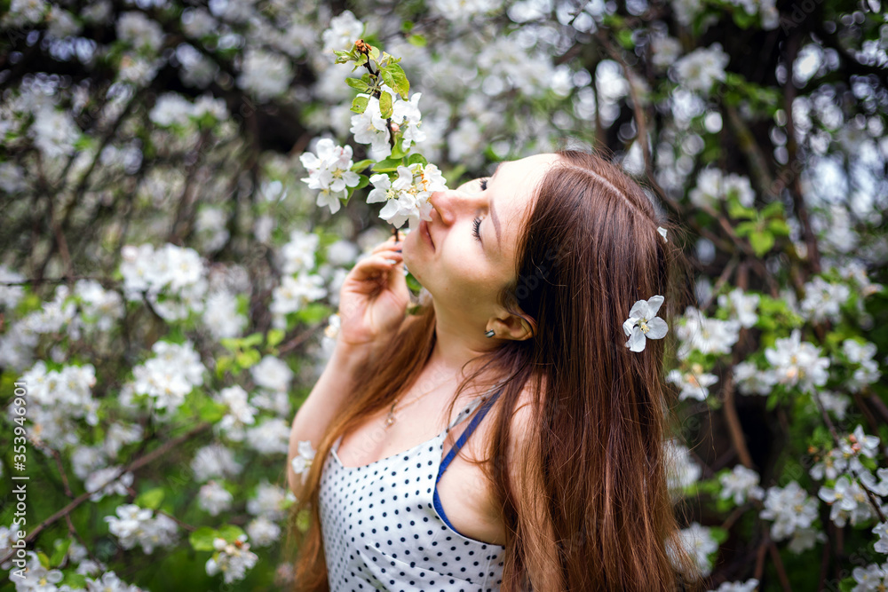 Beautiful long hair girls are developing in the movement. A model with beautiful hair in a spring dress. Sexy girl on the background of blooming Apple trees. Natural hairstyle.