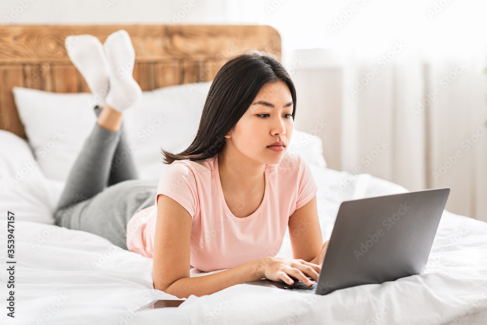 Asian Woman With Laptop Working Distantly Lying In Bed Indoors Asian Woman With Laptop Working Distantly Lying In Bed Indoors
