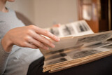 girl in a gray jacket holds an old photo album with black and white photos on her lap and looks at them sitting on the sofa