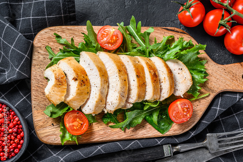 Grilled chicken breast. Chicken fillet and fresh vegetable salad with tomatoes and arugula leaves.  Black background. Top view