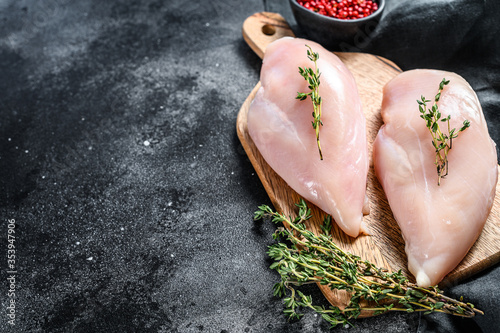Raw chicken breast fillet on a chopping Board with herbs and spices. Black background. Top view. Copy space