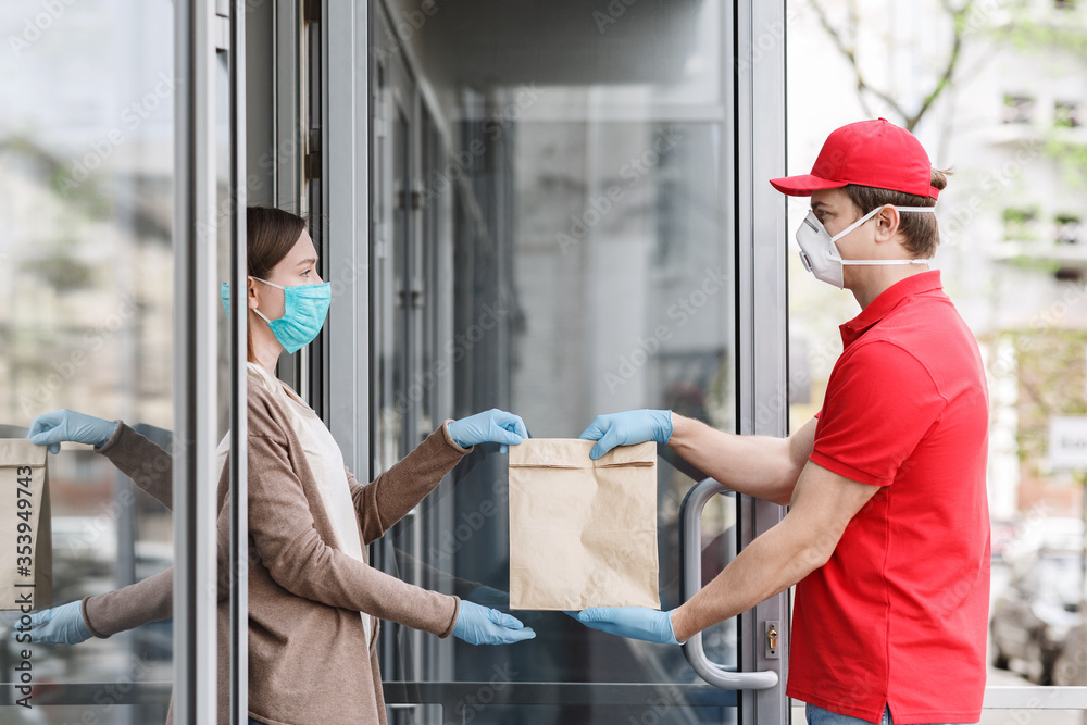 Courier in medical mask and gloves transfers package to customer at home. Courier in medical mask and gloves transfers package to customer at home.