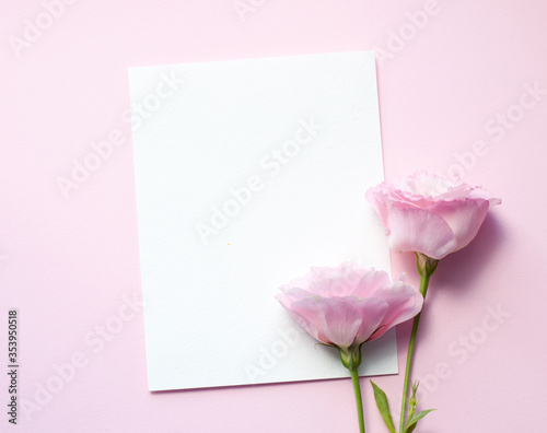 A sheet of paper lies horizontally on pink paper, flowers of eustoma (lisianthus) Top view, Copy space. Concept Mother's Day, Family Day, Valentine's Day
